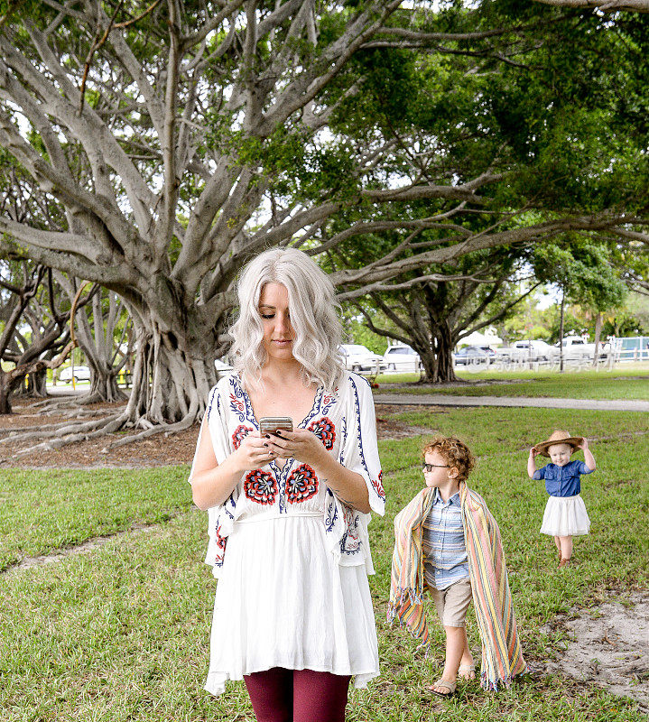 漂亮的白人女人带着孩子在公园散步。她在玩手机，发短信或发邮件，孩子们跟在她后面/她一直在玩手机，没有注意到孩子们